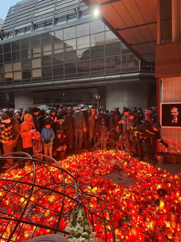 A group of people standing outdoors around a large collection of small brightly-lit red-orange candles