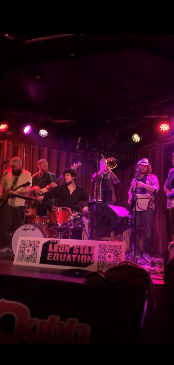 Photo of a full band playing music on stage in dim bar
