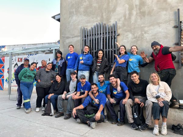 A group of people sitting and standing next to a large wall and smiling at the camera