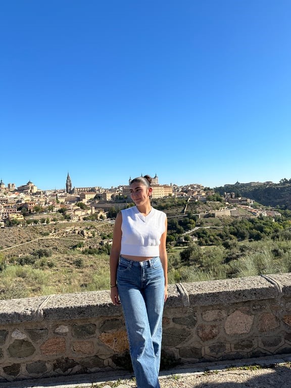 A study abroad student standing on a stone wall with a city in the background.