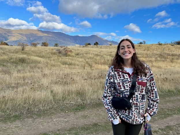 A study abroad student standing in a field with mountains in the back