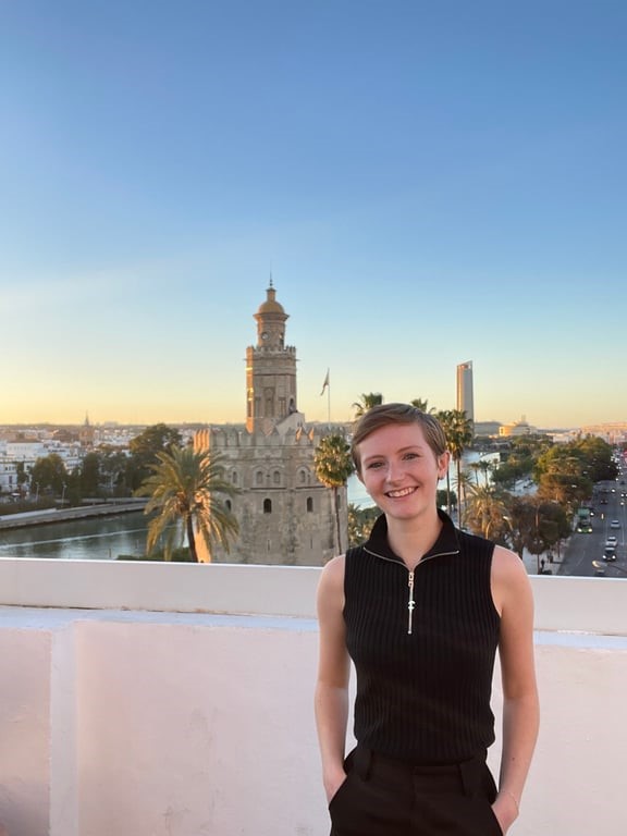 A study abroad student standing on a balcony with a city in the background.
