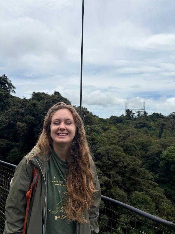 A study abroad student with long brown wavy hair standing outdoors and smiling at the camera