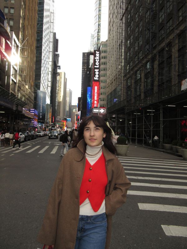 A study abroad student standing outdoors on a city street sidewalk and smiling while looking slightly away from the camera