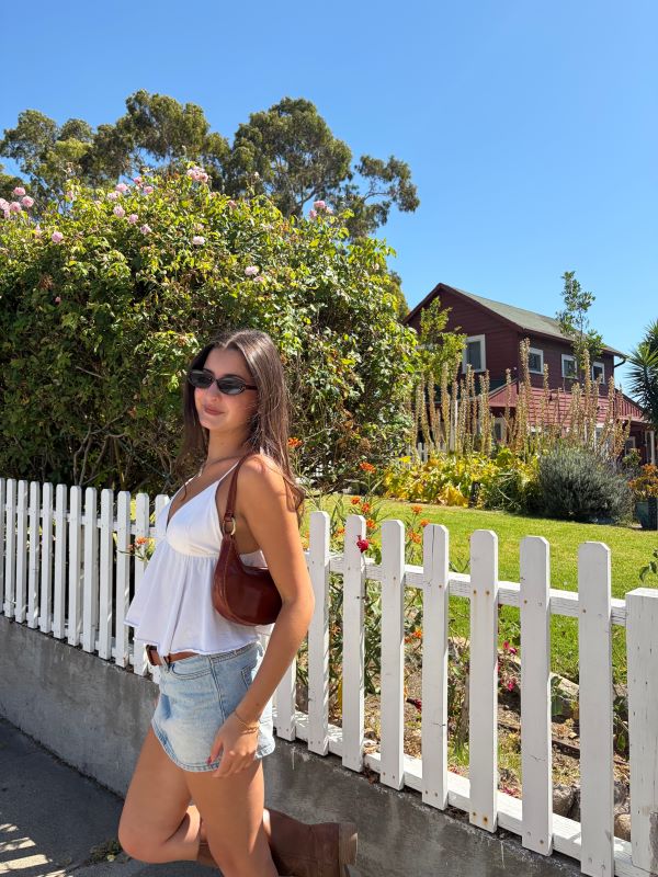 A study abroad student wearing sunglasses standing outdoors and smiling while turned slightly away from the camera