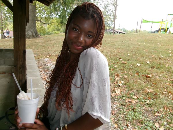 A study abroad student sitting outdoors and holding a white styrofoam cup while smiling at the camera