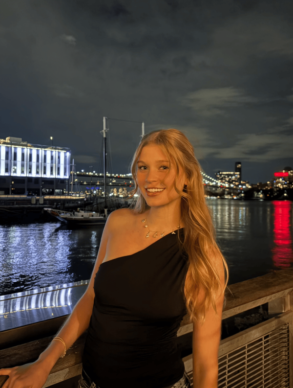 A study abroad student with long wavy blonde hair standing outdoors at night and smiling at the camera