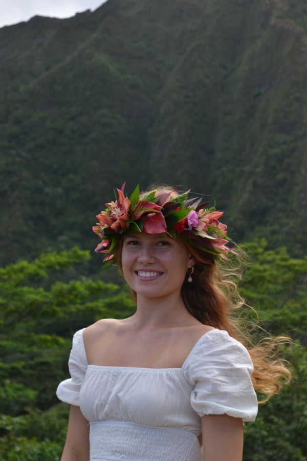 A study abroad student wearing a brightly-colored flower crown around their head and smiling at the camera in an outdoor setting