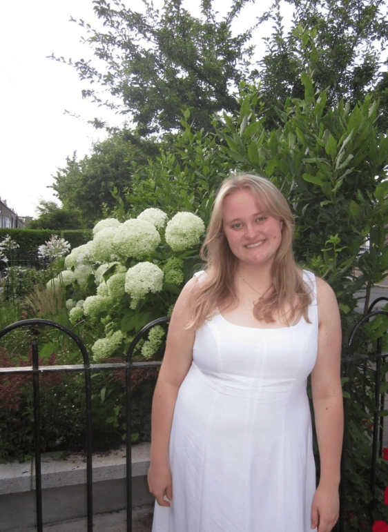 A study abroad student wearing a white dress smiling at the camera while standing outdoors