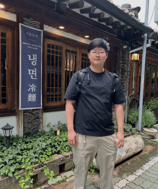 A study abroad student wearing glasses and a backpack standing outdoors while smiling at the camera