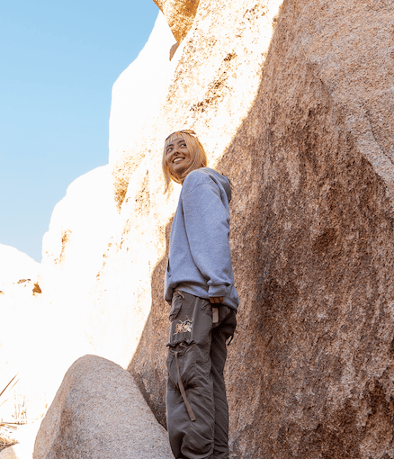 A study abroad student standing outdoors in front of a large rock formation and smiling while looking slightly away from the camera