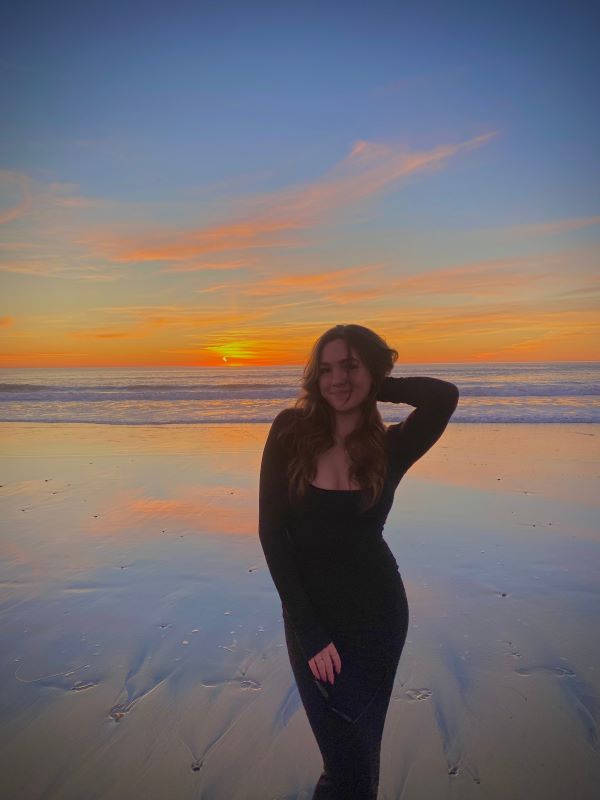 A study abroad student smiling at the camera while standing in front of a body of water with one hand behind their head