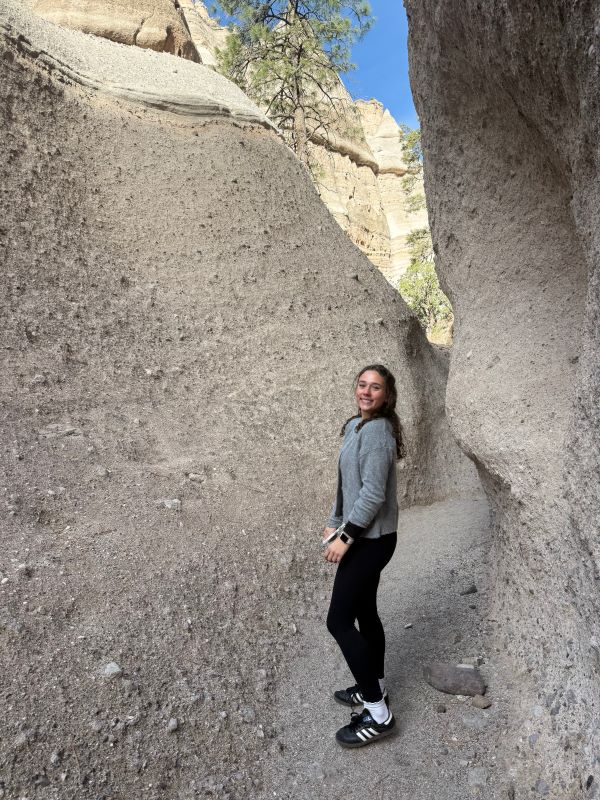 A study abroad student standing between two tall rocky walls outdoors and smiling at the camera