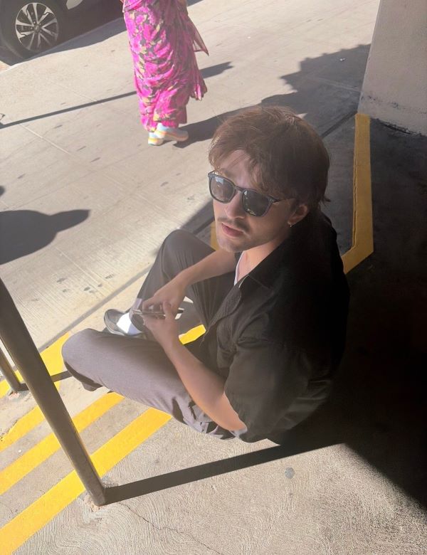 A study abroad student wearing sunglasses as seen from above sitting on a staircase outdoors and looking up at the camera