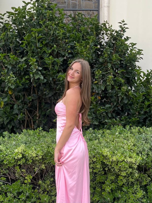 A study abroad student wearing a long pink dress smiling at the camera outdoors while turned slightly to the side
