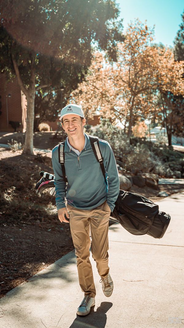 A study abroad student standing outdoors and wearing a golf bag on their back while smiling at the camera
