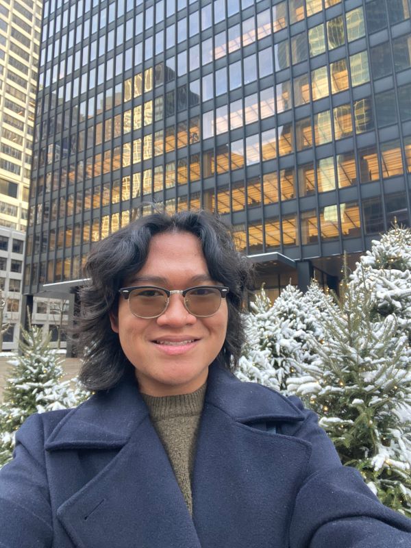 A study abroad student wearing glasses and a winter coat smiling at the camera in an outdoor setting