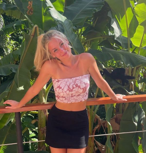 A study abroad student standing outdoors and smiling at the camera in front of a leafy green background